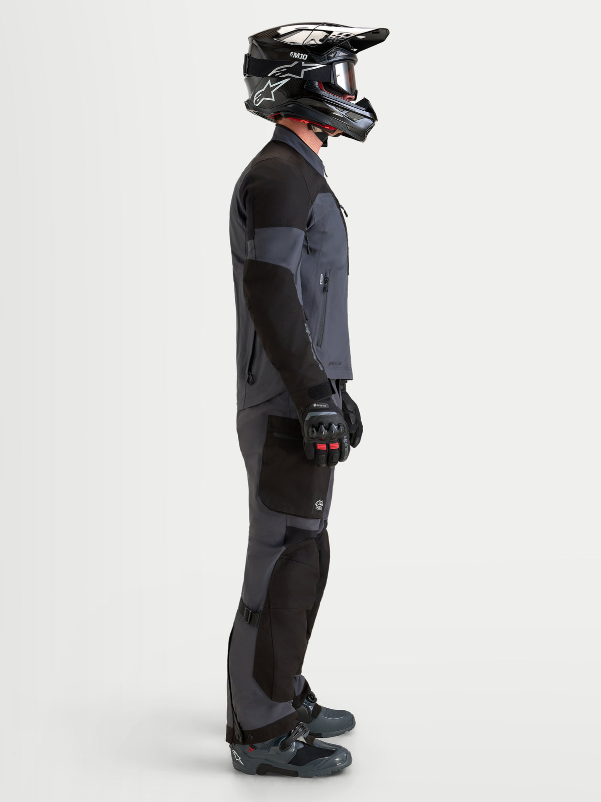 Alpinestars Arenis Gore-Tex Gear Set, adventure motorjas en motorbrook voor heren in zwart en donkergrijs, zijaanzicht op model met bijpassende helm en laarzen, waterdichte all-terrain motorkleding