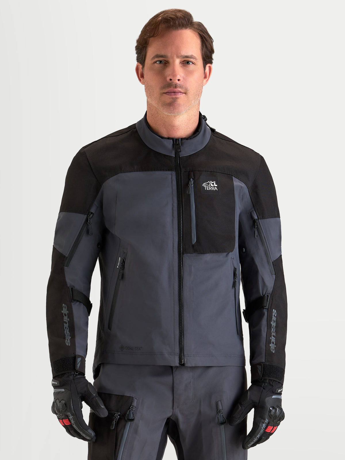 Alpinestars Arenis Gore-Tex jas, avontuurlijke motorjas voor heren in zwart en donkergrijs, vooraanzicht op model met bijpassende uitrusting en handschoenen, CE-gecertificeerde waterdichte all-terrain motorkleding
