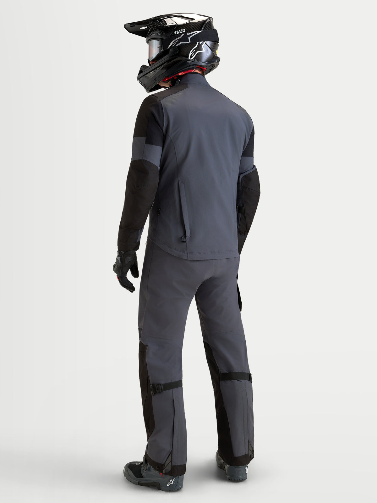 Alpinestars Arenis Gore-Tex Gear Set, heren adventure motoruitrusting in grijs en zwart, achteraanzicht op een model met bijpassende uitrusting en helm, waterdichte all-terrain motorkleding