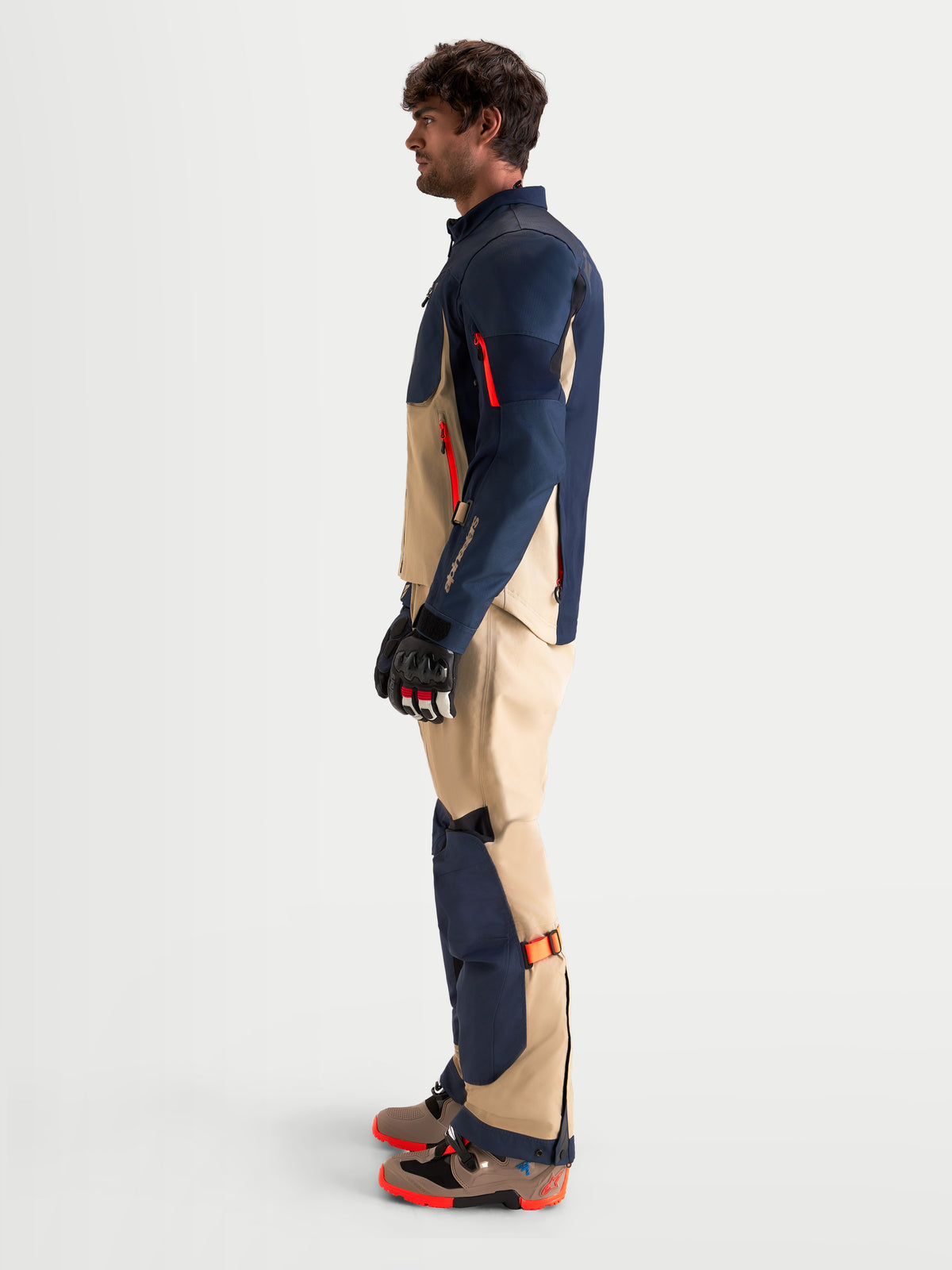 Alpinestars Arenis Gore-Tex® Tenue complète, ensemble veste et pantalon de moto adventure pour homme en bleu marine et beige, vue de profil latéral porté par un modèle avec des gants et des bottes assortis, équipement de conduite tout-terrain imperméable certifié AA