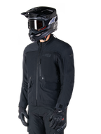 Alpinestars ST-7 Prime GORE-TEX Jacke, schwarze Motorradjacke, getragen von einem Fahrer mit schwarzem Helm und Brille, mit großen Cargo-Taschen auf der Brust und einer laminierten wasserdichten Außenschicht, erstklassige Adventure-Touring- und Pendler-Ausrüstung.