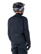 Alpinestars St-7 Prime GORE-TEX Jacke, Schwarz, Rückansicht eines Fahrers, der die Jacke mit passendem Helm und Hose trägt, mit Alpinestars-Branding und geografischen Koordinaten am unteren Rücken.