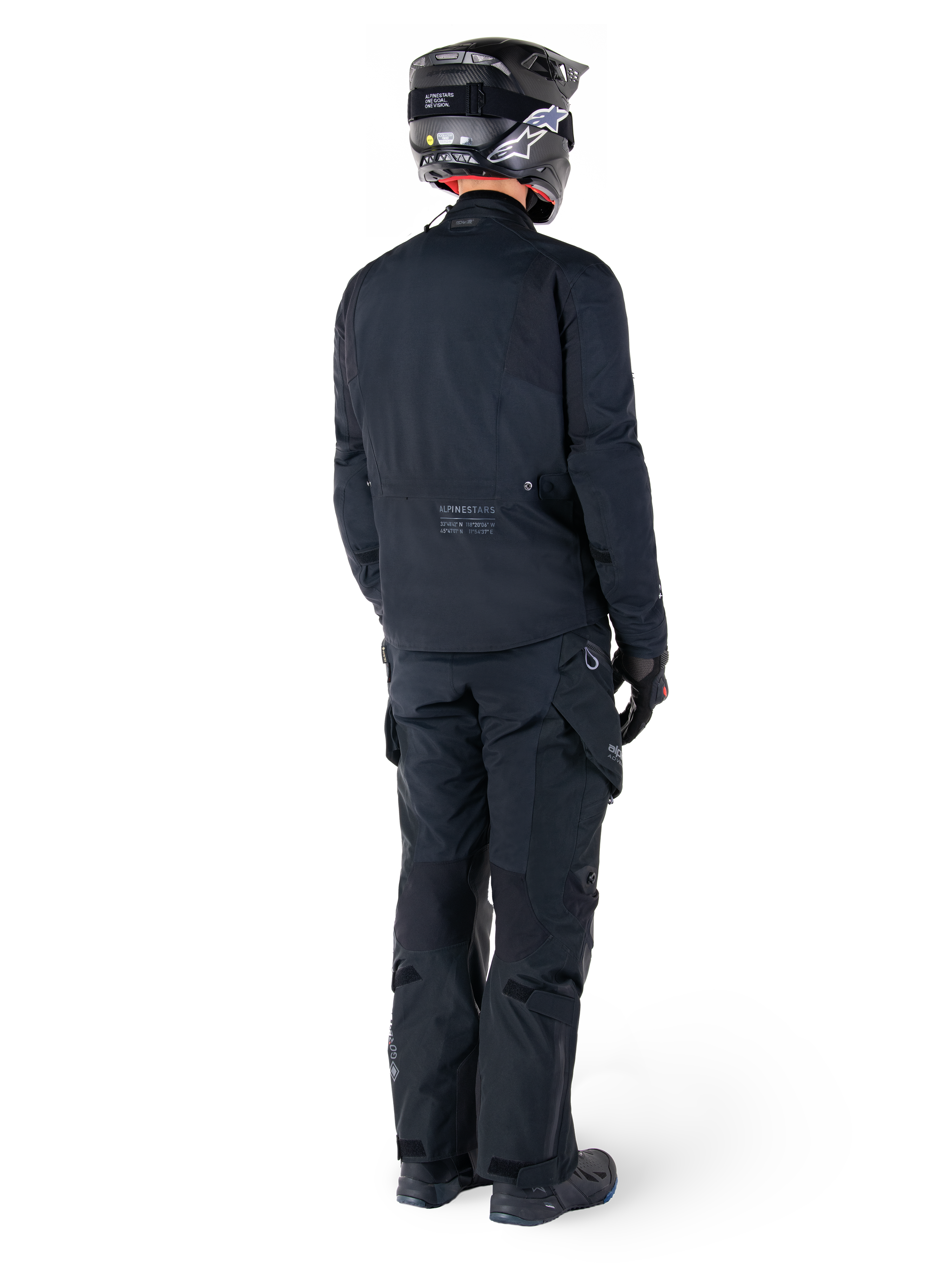 Rückansicht eines Fahrers mit der Alpinestars St-7 Prime GORE-TEX Jacke in Schwarz, kombiniert mit einer passenden schwarzen Tourenhose, einem schwarzen Motorradhelm mit weißem Logo und schwarzen Motorradstiefeln, komplette Adventure-Schutzausrüstung für Touren und Pendelfahrten.