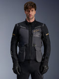 Alpinestars ST-7 2L GORE-TEX jas, heren adventure touring motorjas, donkergrijs en zwart met khaki accenten, voorzien van 'Alpinestars Exploration Equipment' branding, waterdichte cargozakken en een hoge kraag, gedragen door een model met zwarte handschoenen