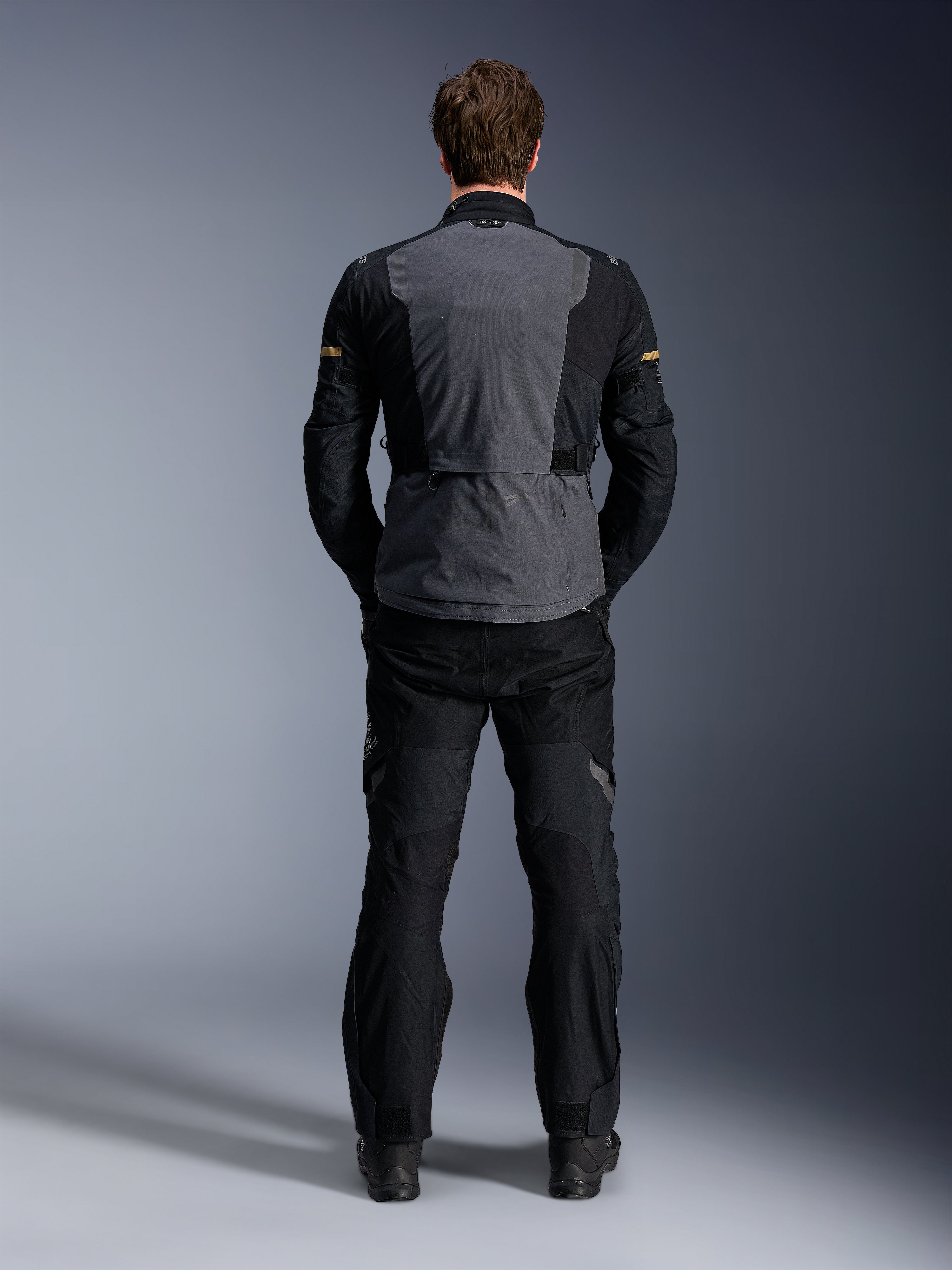 Alpinestars ST-7 2L GORE-TEX jas, Deep Gray Black en Dark Khaki, achteraanzicht op een model, adventure motor touringjas met grijs rugpaneel en zwarte voorgevormde mouwen, gedragen met bijpassende zwarte broek