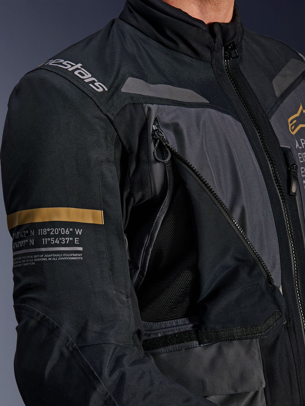 Alpinestars ST-7 2L GORE-TEX Jas, donkergrijs en zwart, close-up van geopend ventilatiepaneel op de borst met rits en mesh, Alpinestars-logo op de schouder en kaki streep op de mouw met geprinte geografische coördinaten, technische adventure-touring motoruitrusting