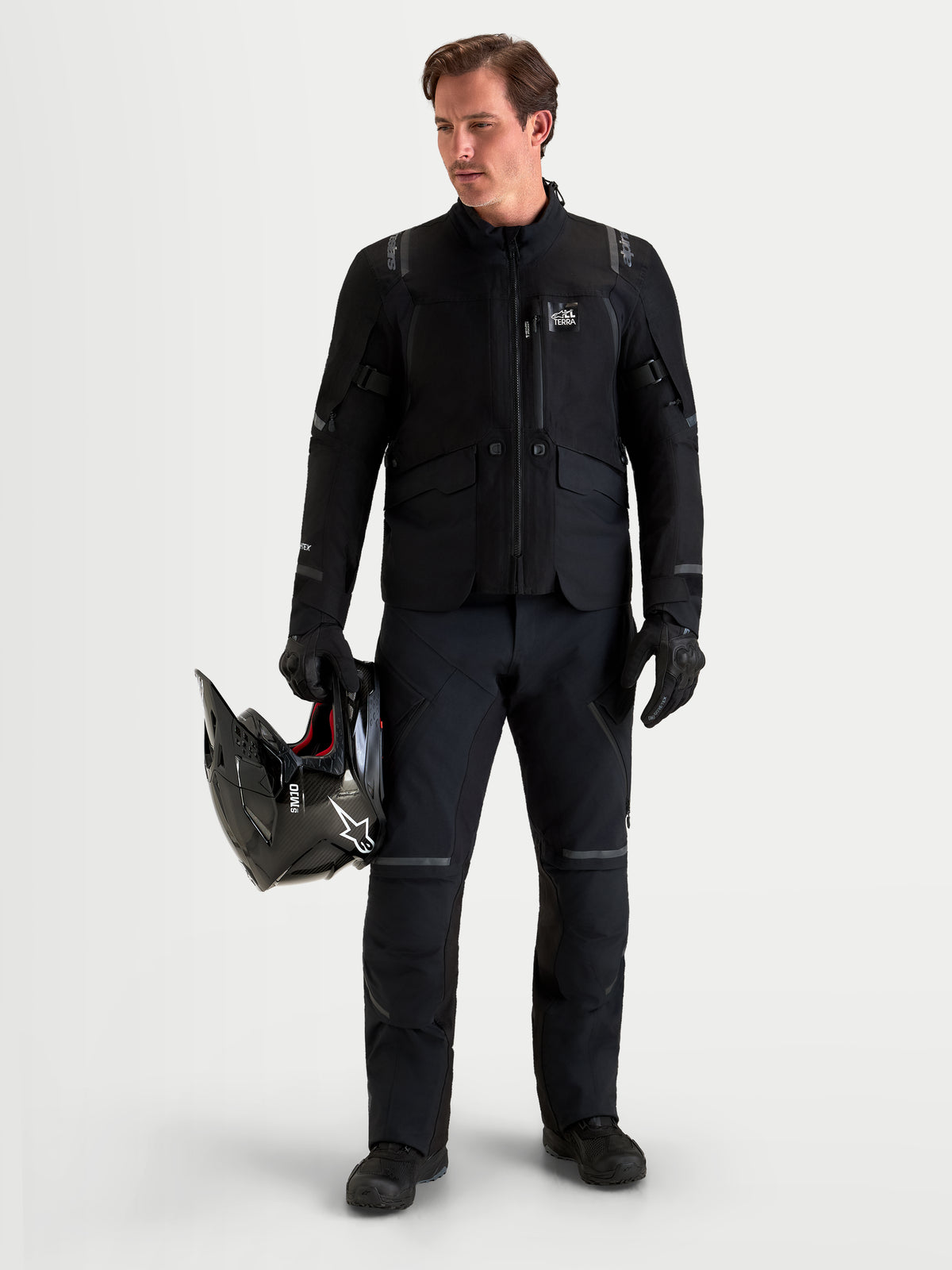 Alpinestars St-7 V2 2L Gore-Tex Pants Short, men's adventure touring motorcycle pants in black, front view on a model wearing matching gear and holding a helmet, AA certified waterproof all-terrain riding apparel.