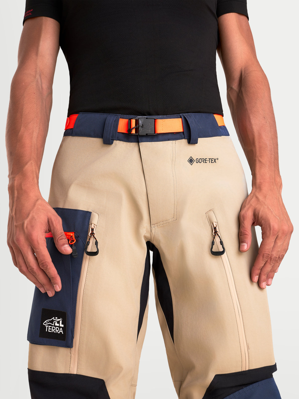 Alpinestars Arenis Gore-Tex Pantalons, pantalon de moto adventure pour homme beige et bleu marine avec ceinture orange, vue rapprochée montrant le marquage GORE-TEX, la boucle magnétique, les aérations aux cuisses et la poche cargo