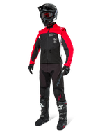 Alpinestars Pro-Dura jas, off-road motorjas, zwart met felrood en wit, gedragen met volledige race-uitrusting inclusief zwarte helm met rode bril, zwarte broek en zwart-witte laarzen, duurzame textiele outfit voor enduro en trailrijden
