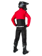 Motocrossrijder van achteren gezien, dragend de Alpinestars Pro-Dura jas in zwart, felrood en wit, gecombineerd met een zwarte broek, zwarte helm en zwarte off-road laarzen, met een rood bovenstuk en een zwart onderstuk met witte Alpinestars-logo's op de rug.