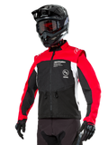 Alpinestars Pro-Dura Jacket, off-road enduro motorjas, zwart met felrood en wit kleurontwerp, gedragen door een rijder met een zwarte helm en crossbril, voorzien van ritszakken aan de voorzijde en Alpinestars-branding, duurzame textielconstructie voor trailrijden