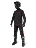 Veste Softshell Lite-Dura Alpinestars, noire, portée par un mannequin avec une tenue complète tout-terrain comprenant un pantalon noir, des bottes noires et blanches, un casque noir avec des lunettes rouges, équipement professionnel de motocross et d'enduro.