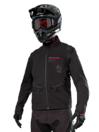 Alpinestars Lite-Dura Softshell Jacket, veste de moto tout-terrain noire avec logos rouges et logo AS, portée avec un casque de motocross noir, des lunettes rouges et des gants noirs, dotée de poches zippées et de poignets réglables, conçue pour l'enduro