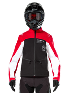 Veste Softshell Alpinestars Lite-Dura en noir, rouge vif et blanc, portée par un pilote de motocross avec un casque noir et des lunettes teintées rouge, dotée d'empiècements blancs sur les manches, du logo Alpinestars sur la poitrine et d'un design sportif tout-terrain.
