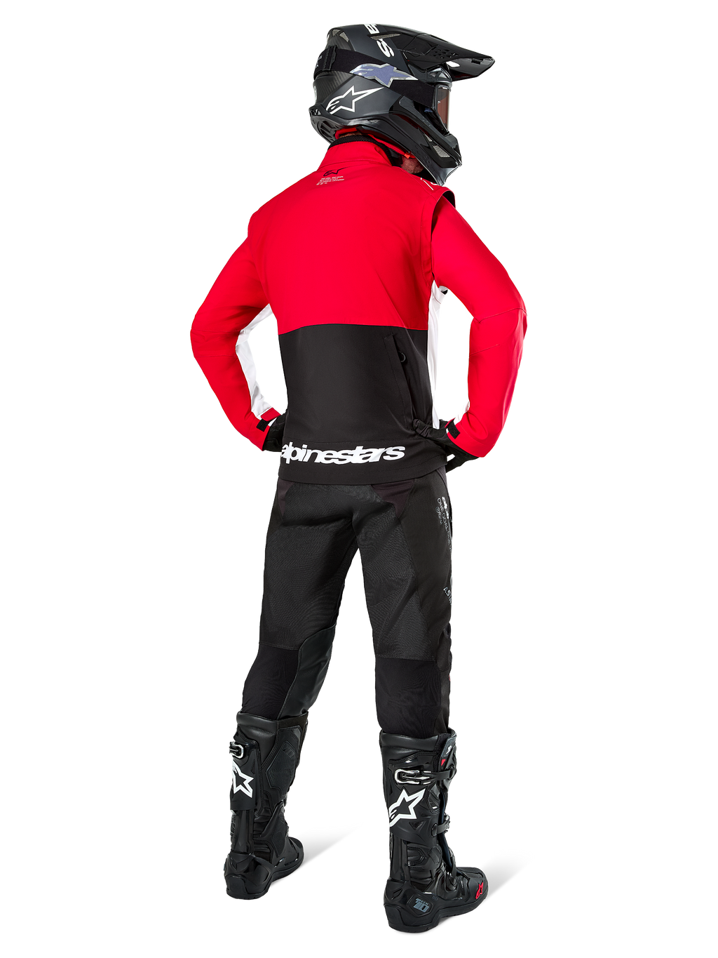 Pilote de motocross vu de dos portant la veste softshell Alpinestars Lite-Dura, noir, rouge vif et blanc, avec un empiècement supérieur rouge et une partie inférieure noire avec logo blanc, associée à un pantalon noir, un casque noir et des bottes noires, tenue d'enduro coordonnée pour la conduite tout-terrain