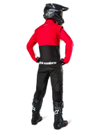 Pilote de motocross vu de dos portant la veste softshell Alpinestars Lite-Dura, noir, rouge vif et blanc, avec un empiècement supérieur rouge et une partie inférieure noire avec logo blanc, associée à un pantalon noir, un casque noir et des bottes noires, tenue d'enduro coordonnée pour la conduite tout-terrain