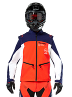 Veste Softshell Alpinestars Lite-Dura en bleu marine, orange vif et blanc, vue de face sur un pilote portant un casque noir et des lunettes, design technique à blocs de couleurs avec poches zippées et logos Alpinestars, équipement polyvalent pour l'enduro et le tout-terrain