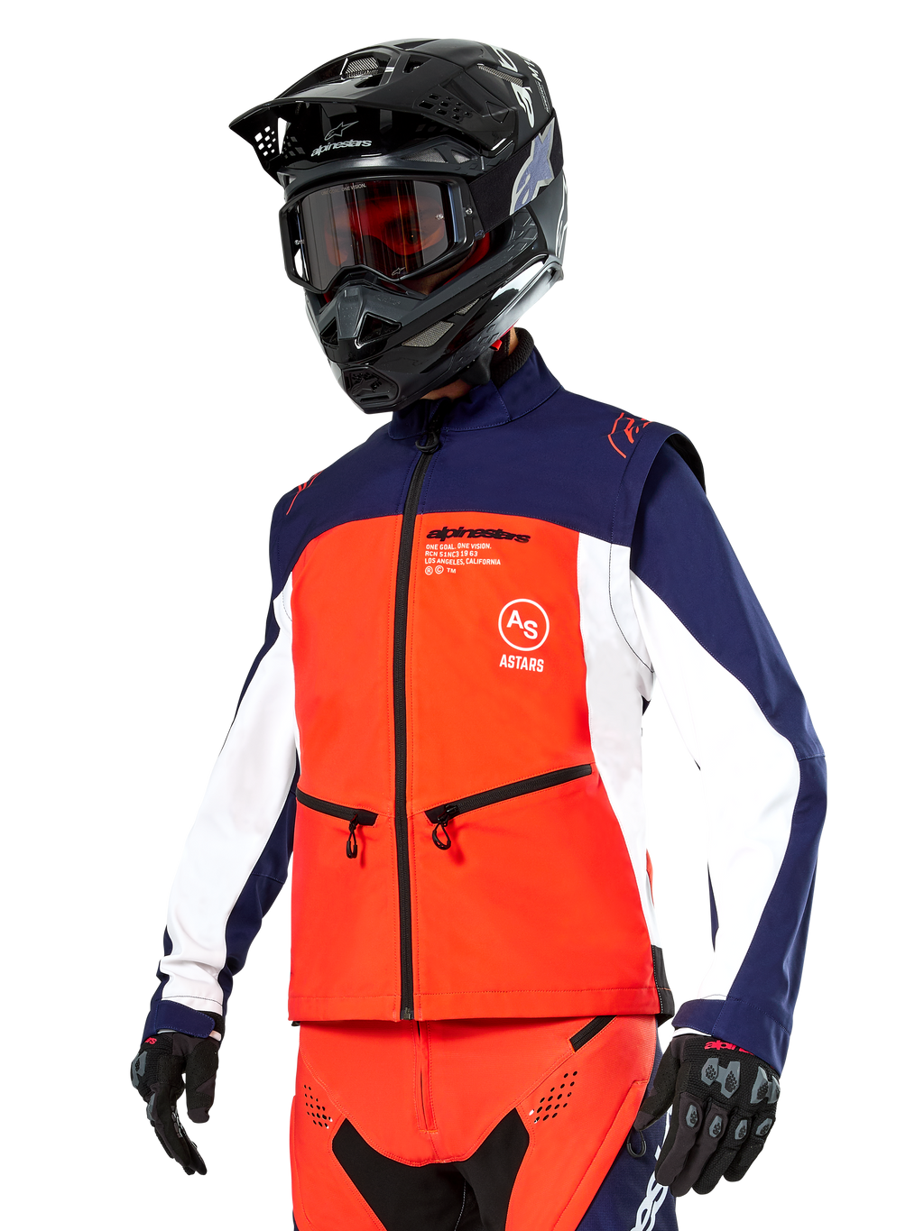 Veste Softshell Alpinestars Lite-Dura en bleu marine, orange vif et blanc, équipement de motocross, portée avec un casque et des lunettes noirs, des gants de protection et un pantalon de course assorti