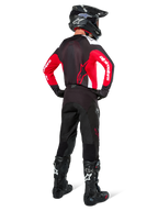 Motocross-Fahrer von hinten in Alpinestars Pro-Dura Hose in Black Magnet White, kombiniert mit einem rot-schwarzen Trikot und schwarzen Stiefeln, abgestimmtes Offroad-Ausrüstungsset für Enduro-Fahrten