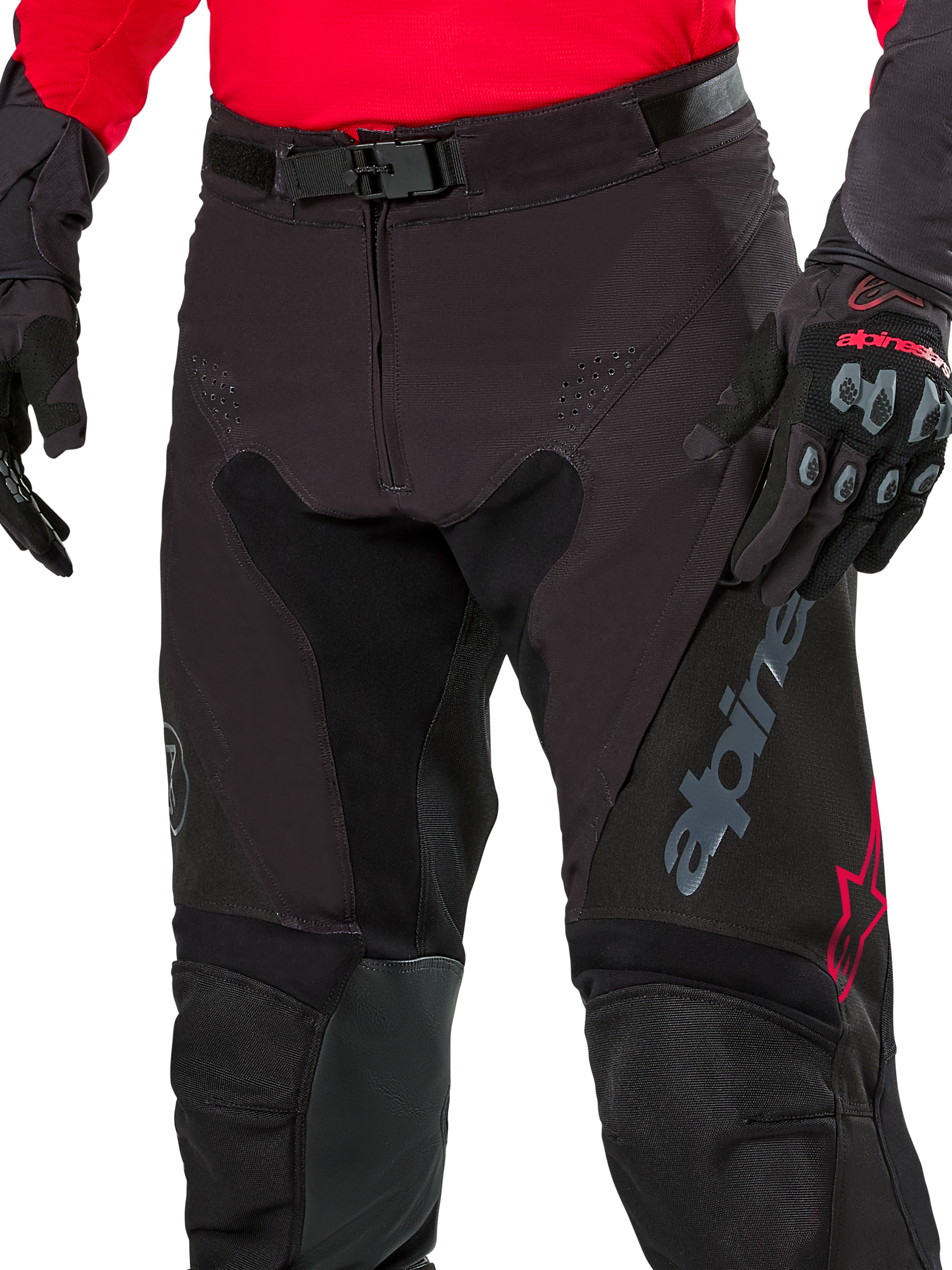 Nahaufnahme der Alpinestars Pro-Dura Hose, Enduro-Hose, Black Magnet White mit roten Akzenten, mit sicherem Magnet-Schnallenverschluss und Reißverschluss, getragen mit passendem rotem Trikot und schwarzen Handschuhen, strapazierfähige Ripstop-Konstruktion für das Offroad-Fahren
