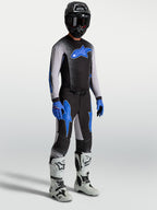 Alpinestars Supertech Hiten AFD-broek, motocrossuitrusting voor heren in zwart en blauw, op model met bijpassende jersey en witte motorlaarzen, professionele off-road raceprestaties.