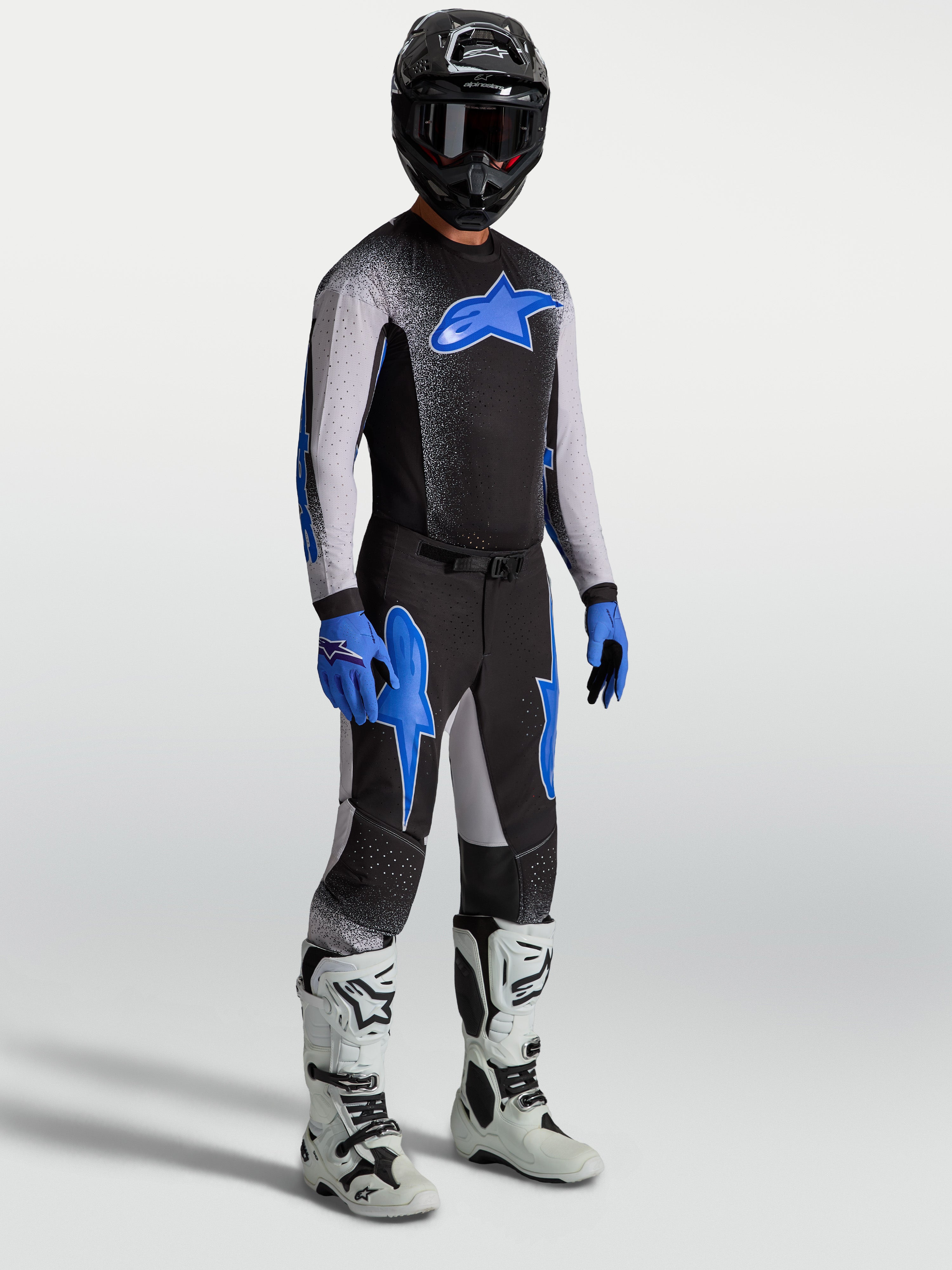 Alpinestars Supertech Hiten AFD-broek, motocrossuitrusting voor heren in zwart en blauw, op model met bijpassende jersey en witte motorlaarzen, professionele off-road raceprestaties.