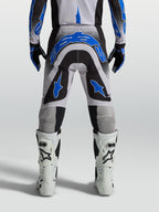 Alpinestars Supertech Hiten AFD broek, herenmotorcrossbroek voor off-road racing, blauw, zwart en wit, atletische racepasvorm, van achteren gezien op een model met witte motorlaarzen.