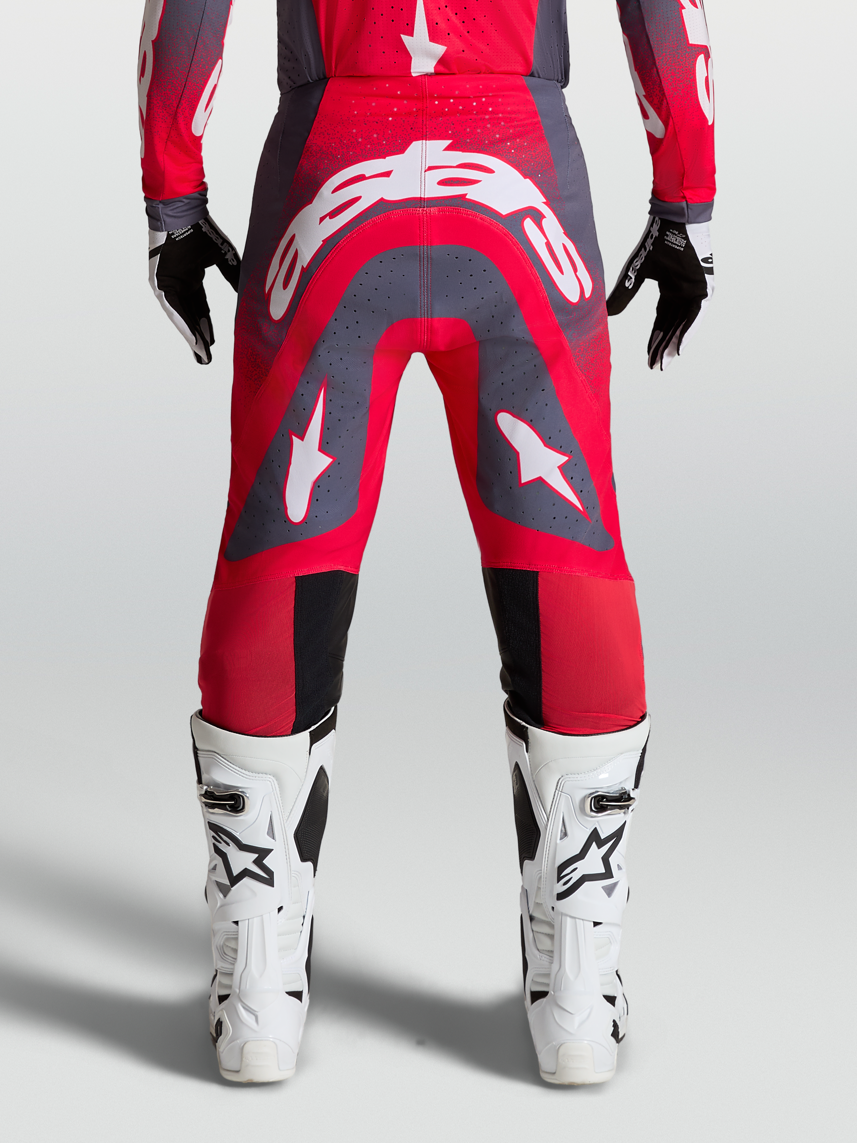 Alpinestars Supertech Hiten AFD Broek, professionele motocrossbroek, rood en grijs met witte logo's, gedragen met witte laarzen.