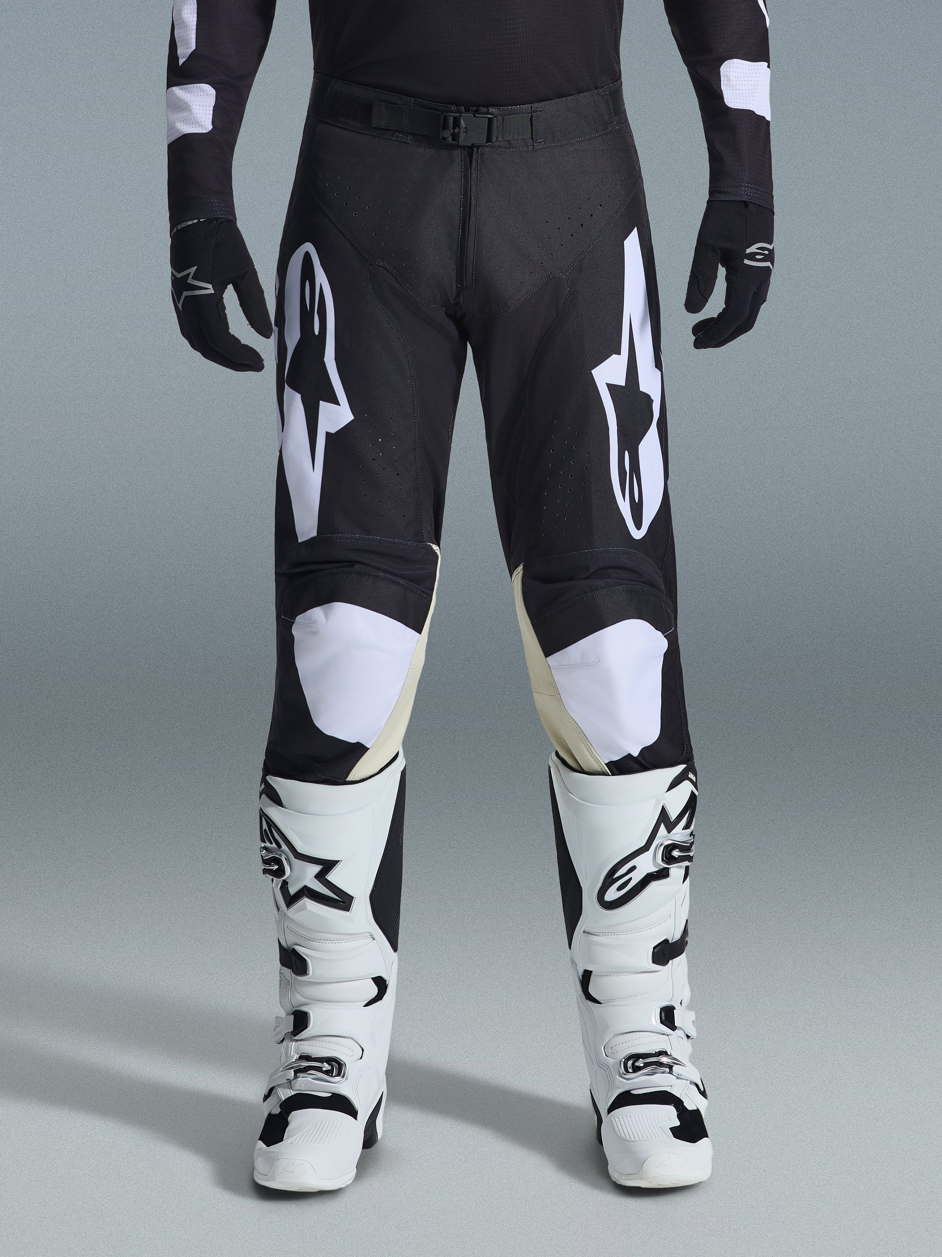 Pantalon Alpinestars Racer Air Riway 2026, pantalon de motocross, noir et blanc, avec des logos Alpinestars blancs sur les cuisses et les genoux, associé à des bottes de motocross blanches et noires et des gants noirs, coupe de course athlétique pour le pilotage tout-terrain