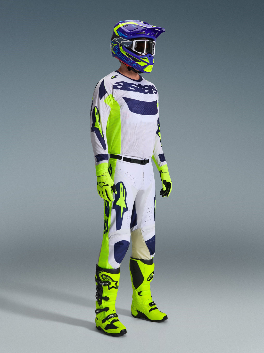 Motocross rider wearing complete racing gear, 2026 Racer Air Riway Pants in Light Gray Yellow Fluo Blue, matching white and blue jersey, fluo yellow gloves and boots, and a blue and yellow helmet, coordinated outfit for professional off-road performance