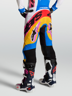 Pantalons Supertech Dyna d'Alpinestars, pantalons de motocross de course en blanc et bleu, portés par un mannequin, dotés de panneaux ventilés et d'une coupe athlétique pour la performance.
