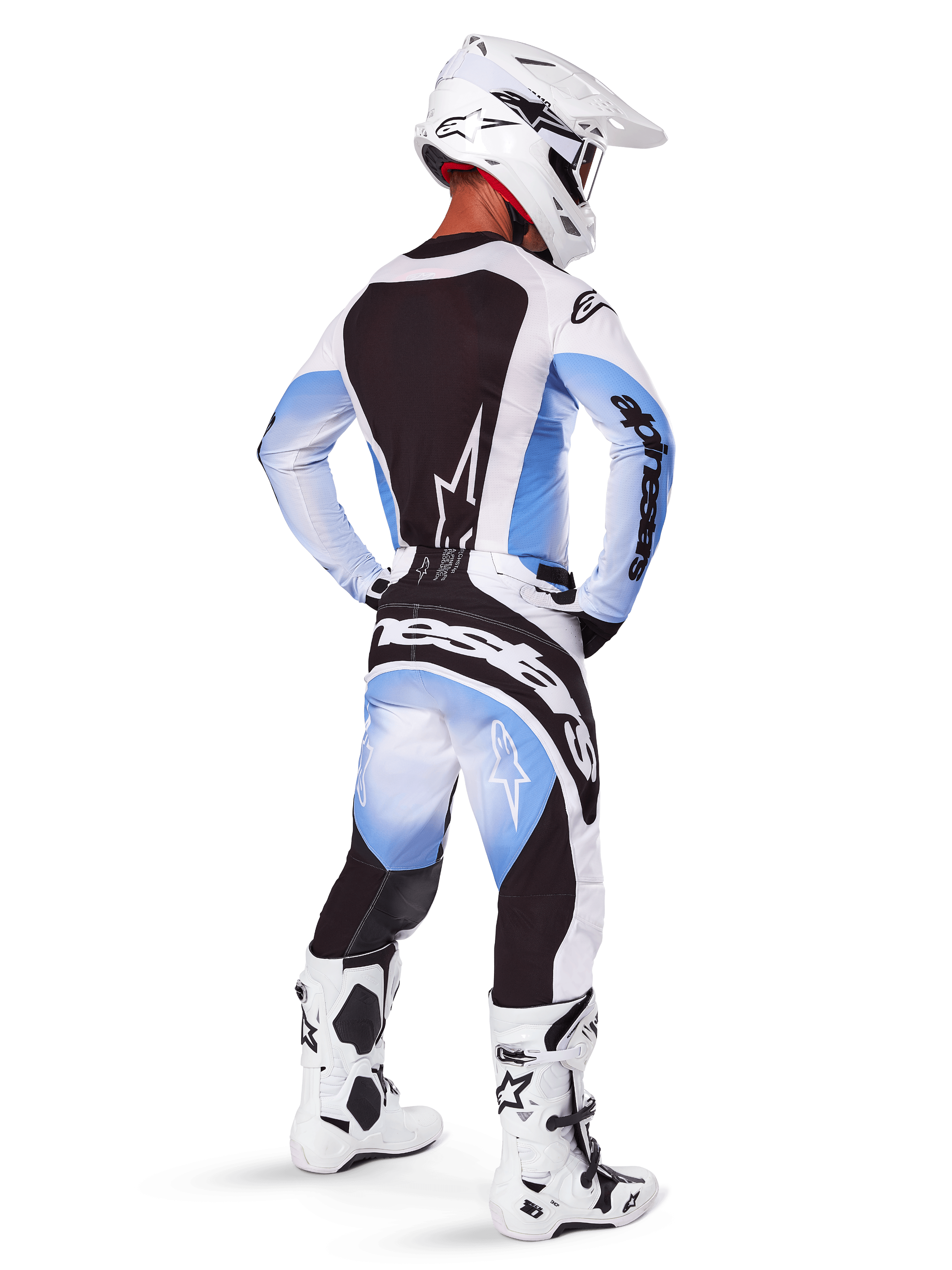 Pilote de motocross vu de dos portant le pantalon et le maillot Alpinestars 2025 Techstar Melt, design dégradé noir, bleu et blanc, casque blanc, bottes blanches et noires, tenue de course tout-terrain complète.