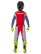 Pilote de motocross portant le pantalon Alpinestars Techstar Melt 2025 rouge vif et gris, avec des empiècements rouge éclatant et des accents jaune fluo, maillot assorti, casque noir et lunettes jaune fluo, bottes et gants jaune vif, tenue de course professionnelle coordonnée
