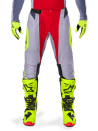 Alpinestars Techstar Melt Pants 2025, pantalon de motocross, rouge et gris avec accents jaune fluo, perforations découpées au laser pour la ventilation, porté avec des gants et des bottes jaune fluo, équipement haute performance pour la course tout-terrain