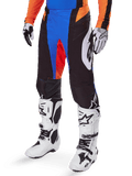 Alpinestars 2025 Techstar Melt broek, motorcrossbroek, zwart met blauwe en oranje accenten, gedragen met witte laarzen en een bijpassende jersey, voorzien van duurzaam beschermend materiaal en een sportief race-ontwerp.