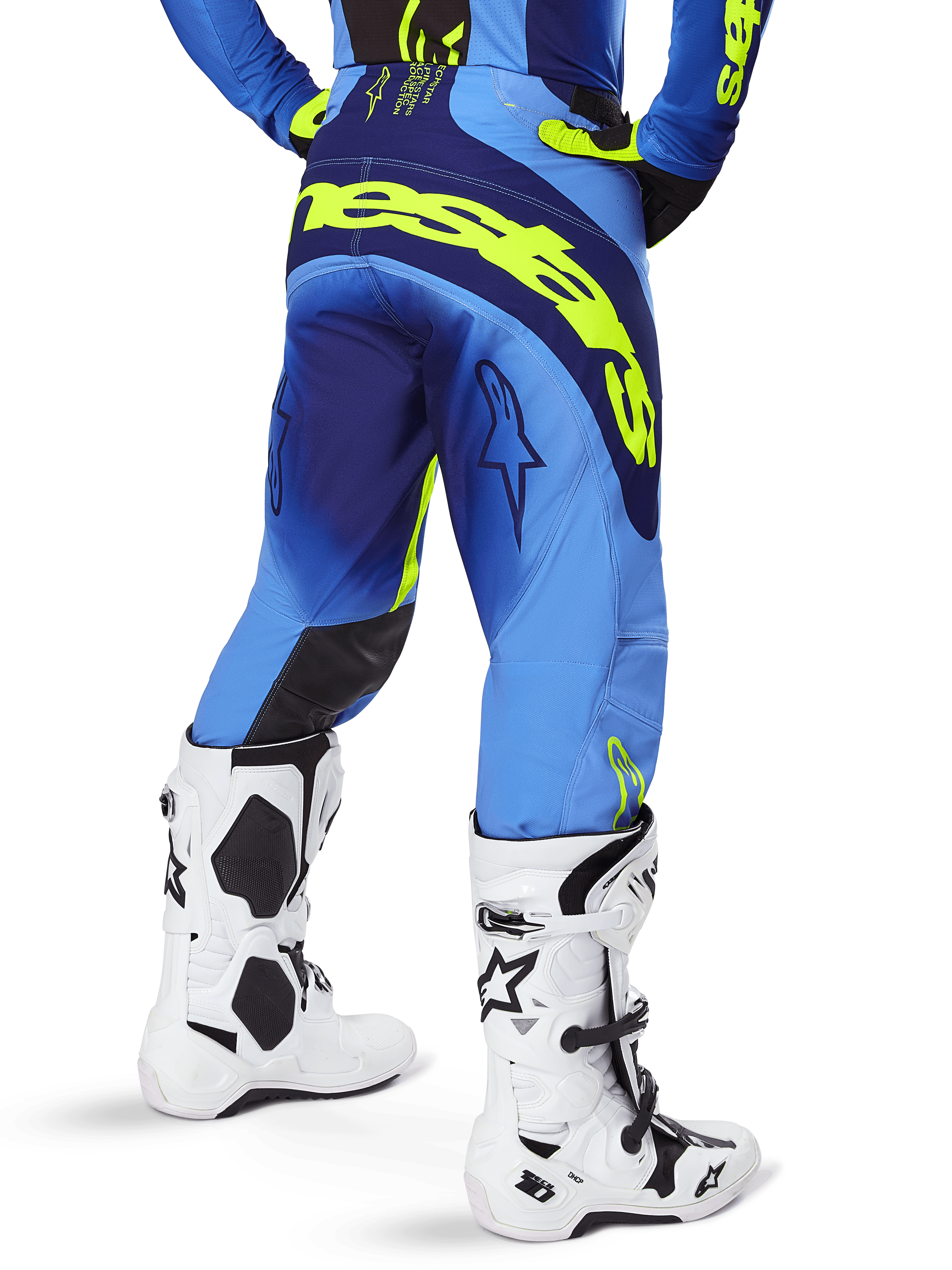 Alpinestars Pantalon Techstar Melt 2025, pantalon de motocross, bleu et jaune fluo, vue arrière montrant le large logo jaune sur l'assise et les cuisses, porté avec des bottes de motocross blanches et un maillot bleu assorti, coupe athlétique pour la conduite tout-terrain