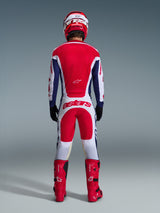 Motocross-Fahrer von hinten in vollständiger Rennausrüstung, Alpinestars 2026 Racer Riway Hose in Weiß, Blau und Rot mit passendem Jersey, roten Stiefeln und Helm, mit großem „astars“-Logo auf der Sitzfläche, koordiniertes Motocross-Outfit.