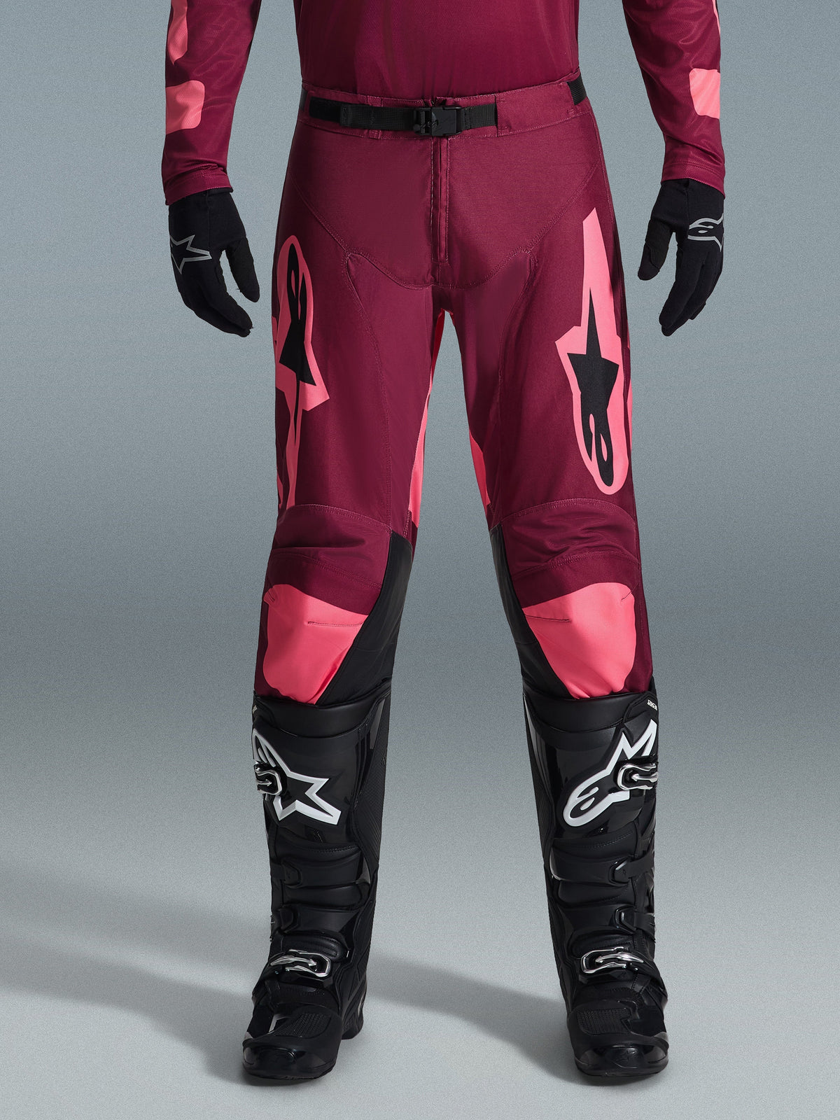 Alpinestars 2026 Racer Riway Hose, Motocross-Hose, Dark Red Coral, getragen mit schwarzen Handschuhen und Stiefeln, mit großen korallenfarbenen Alpinestars-Logos auf den Oberschenkeln, schwarzer Taillenschnalle und vorgeformtem Beindesign für Offroad-Rennsport