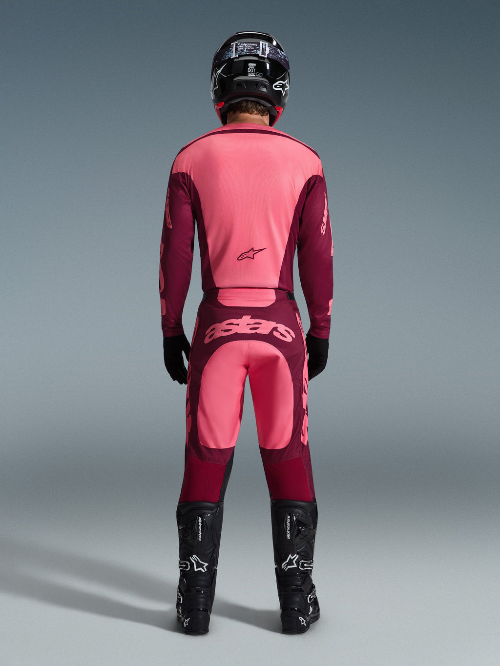 Motocross rider from the back wearing Alpinestars 2026 Racer Riway Pants in Dark Red Coral, matching jersey, black helmet, black gloves, and black Alpinestars boots, featuring a bold 'astars' logo on the seat and a two-tone red design.