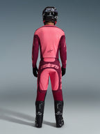 Rückansicht eines Motocross-Fahrers im 2026 Racer Riway Gear Set, pink- und bordeauxrotes Trikot, passende bordeauxrote Hose mit hellpinkem 'astars'-Logo auf dem Gesäß, schwarzer Helm, schwarze Stiefel und schwarze Handschuhe, abgestimmtes Outfit für Offroad-Performance