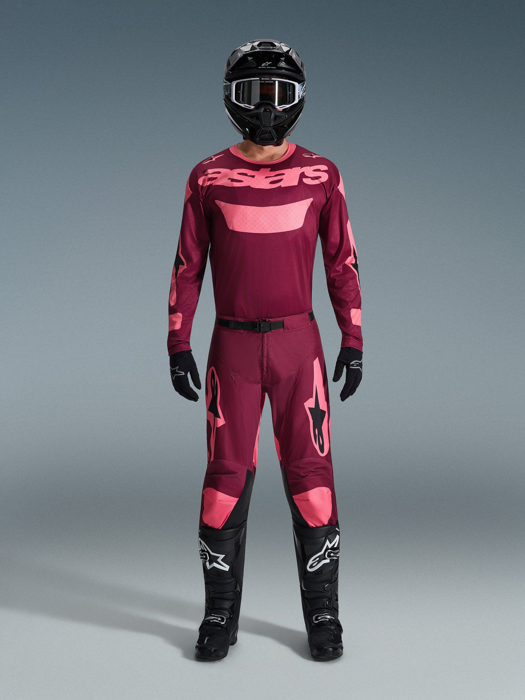 Motocross rider wearing complete racing gear, Dark Red Coral jersey with pink accents, matching Racer Riway pants, black helmet with white details, black boots with white logos, black gloves, coordinated outfit for off-road racing
