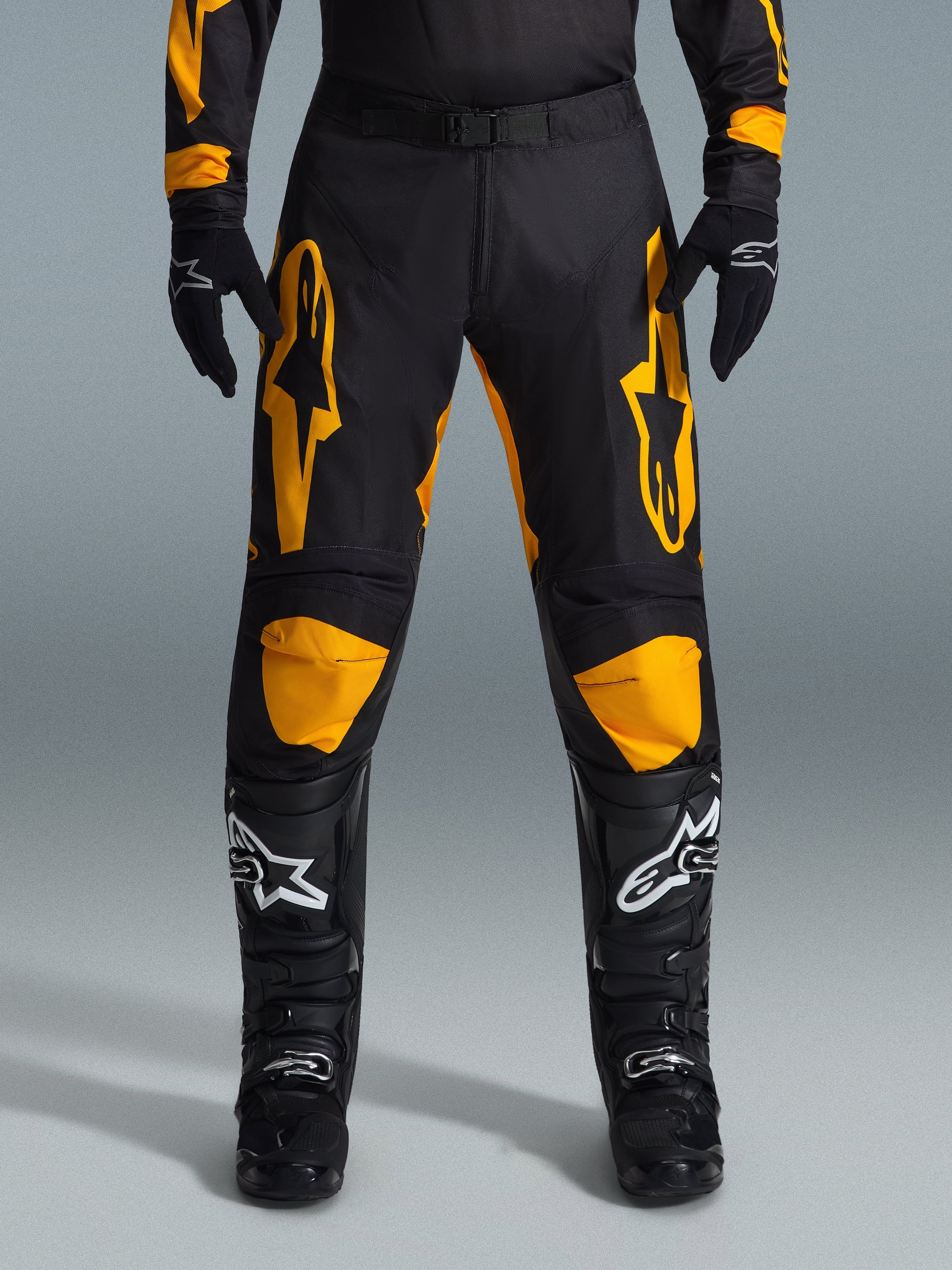 Pantalon Alpinestars Racer Riway 2026, pantalon de motocross, jaune et noir, porté avec des gants de motocross noirs et des bottes noires aux logos blancs, arborant de grands logos Alpinestars jaunes sur les cuisses et des empiècements jaunes aux genoux, conception durable pour la performance en course tout-terrain