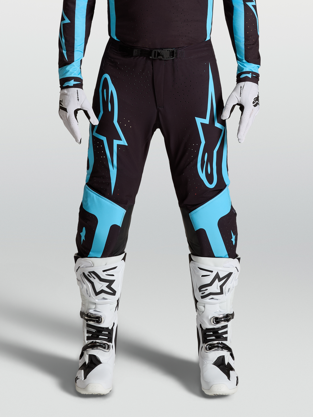 Alpinestars Supertech Vesta broek, professionele motocrossbroek, zwart en turquoise, gedragen door racer met witte laarzen en handschoenen.