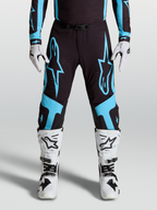Alpinestars Supertech Vesta broek, professionele motocrossbroek, zwart en turquoise, gedragen door racer met witte laarzen en handschoenen.