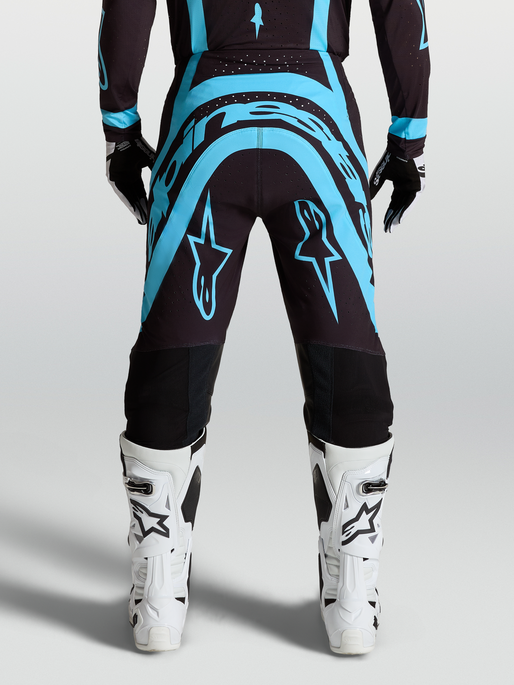 Alpinestars Supertech Vesta Broek, motocrossbroek in zwart en turquoise met witte motorlaarzen, race-fit.