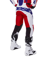 Alpinestars 2025 Racer Veil Hose, Motocross-Hose, Hellrot und Weiß mit blauem Branding, Rückansicht mit schwarzen Stretch-Belüftungseinsätzen an der Beinrückseite, kombiniert mit weißen Motocross-Stiefeln.