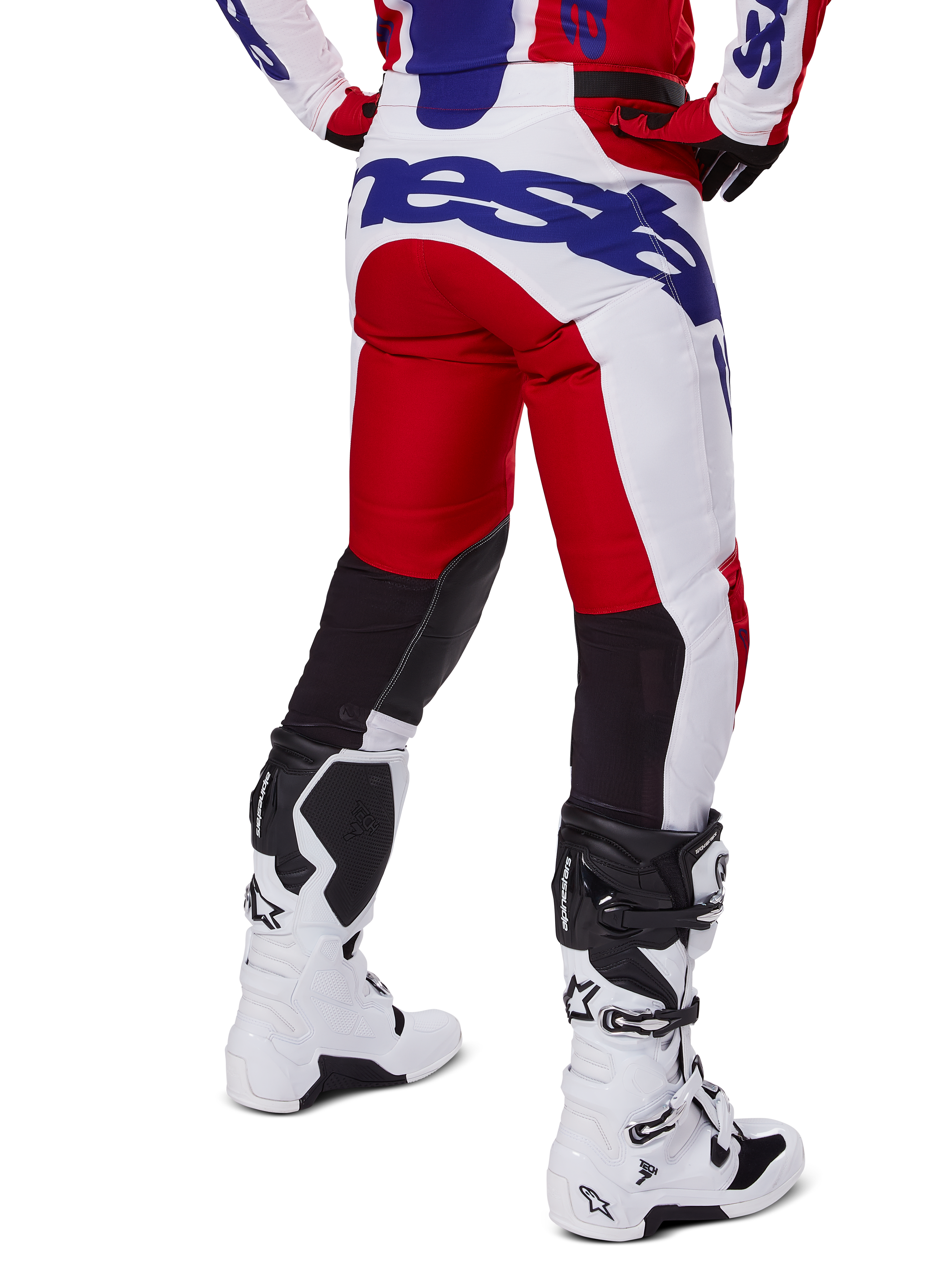 Alpinestars 2025 Racer Veil Hose, Motocross-Hose, Hellrot und Weiß mit blauem Branding, Rückansicht mit schwarzen Stretch-Belüftungseinsätzen an der Beinrückseite, kombiniert mit weißen Motocross-Stiefeln.