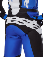 Alpinestars 2025 Racer Veil broek, motorcrossbroek, blauw en zwart, close-up achteraanzicht met een groot wit Alpinestars-woordmerk op het zwarte zitvlak, gedragen met bijpassende blauwe en zwarte uitrusting voor een gecoördineerde off-road look.