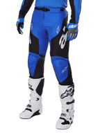 Alpinestars 2025 Racer Veil broek, motorcrossbroek, blauw en zwart met witte grafische accenten, gedragen met bijpassende blauwe jersey, handschoenen en witte laarzen, duurzame beschermende uitrusting voor off-road racen