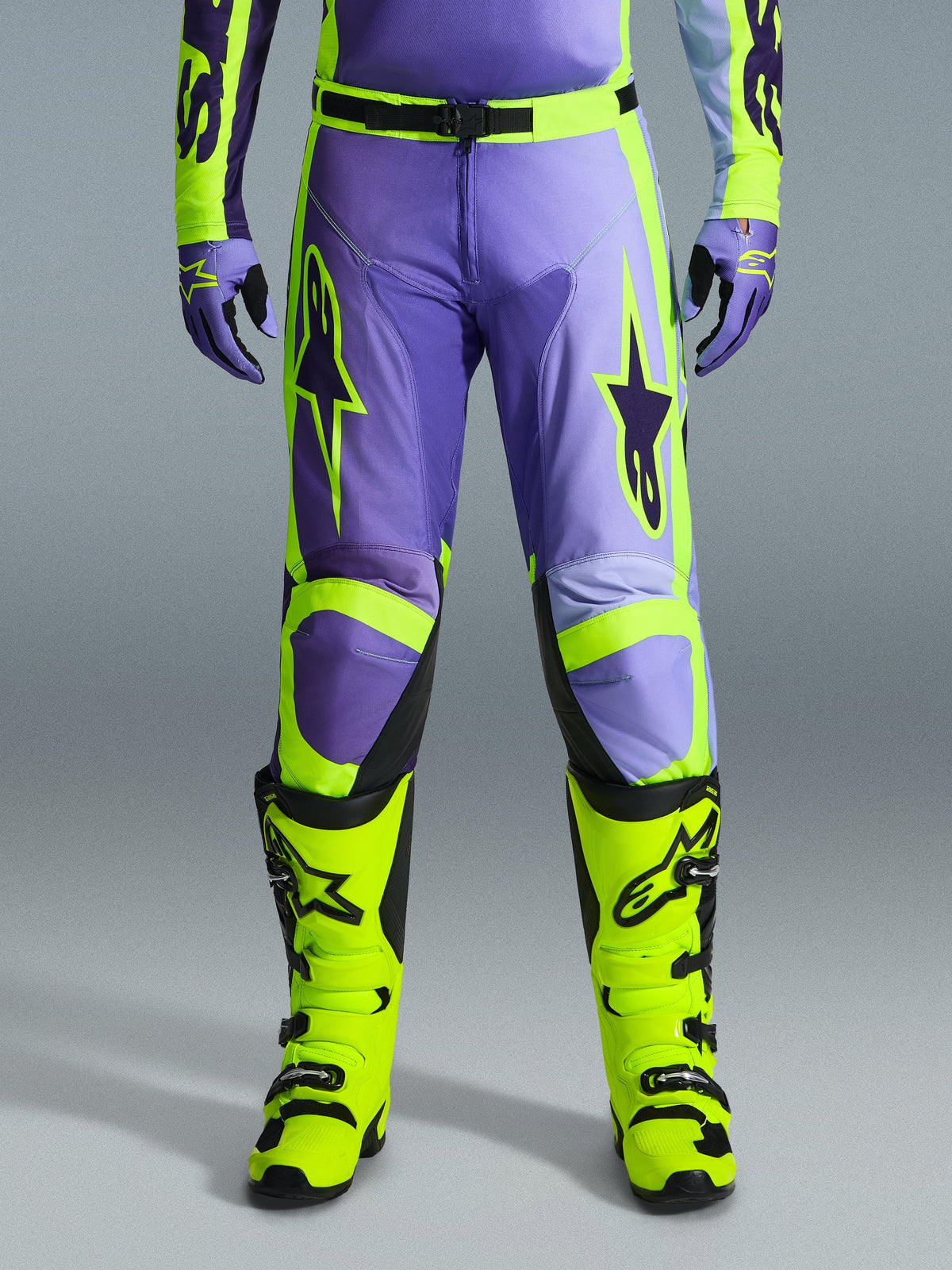 Pantalon Alpinestars 2026 Racer Portl, pantalon de motocross, violet et jaune fluo, porté avec des bottes jaune fluo et des gants violets assortis, arborant de grands logos étoilés et une construction en poly-tissu durable pour la course tout-terrain